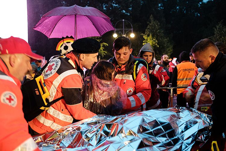 Einsatz von ehrenamtlichen Helfern des DRK-Sanitätsdienstes beim Public Viewing auf der Fanmeile zur Fußball-Weltmeisterschaft 2018: Eine Besucherin wird von Helfern auf eine Trage gelegt, 17. Juni 2018         