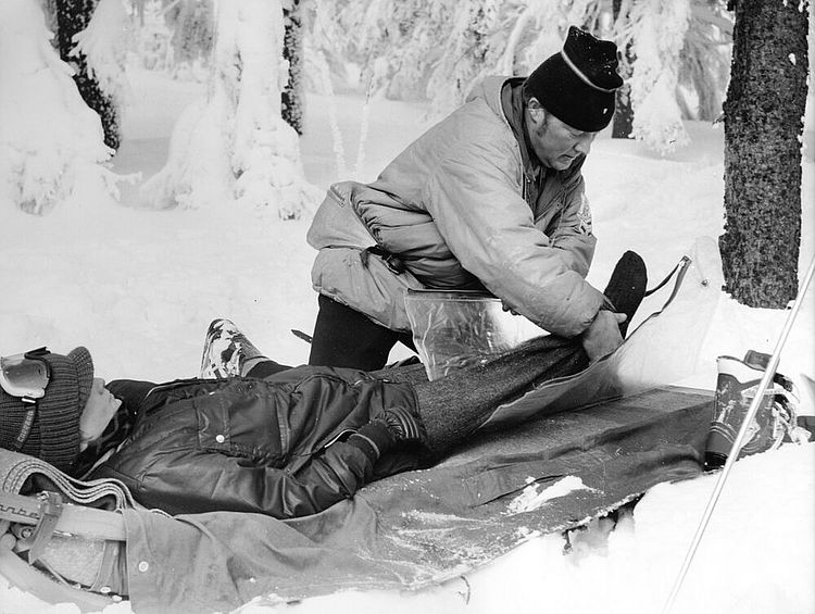 DRK der DDR: Übung des Bergunfalldienstes im Schnee. Eine Person, die einen Unfall hatte, wird für den Abtransport vorbereitet und gegen Kälte und Feuchtigkeit geschützt, 1980er Jahre